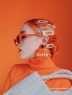 a woman with red glasses and pearls on her head is wearing an orange sweater that says betty