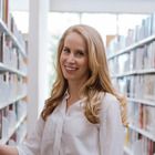 a woman is standing in front of bookshelves and smiling at the camera while she holds out her hand