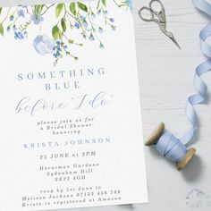 a white card with blue flowers on it next to some scissors and ribbon tied around it