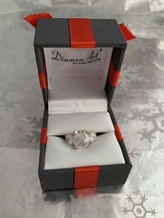 an engagement ring in a gift box with red ribbon around the band and center stone