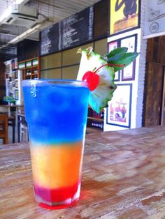 a colorful drink sitting on top of a wooden table next to a slice of pineapple