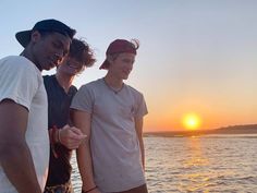 three young men standing next to each other in front of the ocean at sunset or sunrise