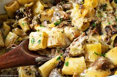 a wooden spoon is in a dish full of pasta and mushrooms with meat, cheese, and parsley