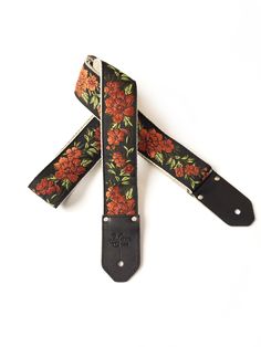 the floral guitar strap is black with orange flowers on it and has two metal buckles