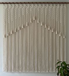 a white curtain with tassels hanging from it's side in front of a plant