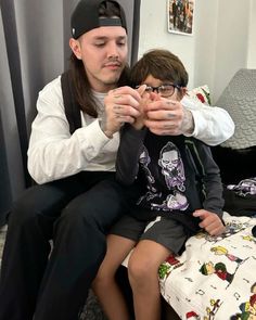 a man sitting on top of a bed next to a little boy holding something in his hands