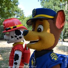 two large stuffed animals dressed in costumes standing next to each other on grass with trees in the background