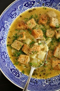 a blue and white bowl filled with soup, bread croutons and parsley