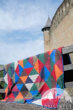 a colorful quilt draped over a wooden bench in front of an old brick wall and castle