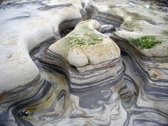 some very pretty rocks with moss growing on them in the middle of water and sand