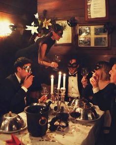 a group of people sitting around a table with candles in front of them and masks on their faces