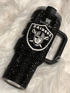 the oakland football team logo is on this black glittered water bottle holder, which sits on a white fur surface