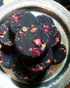 some black cookies with pink flowers on them in a silver plate and saucer, ready to be eaten