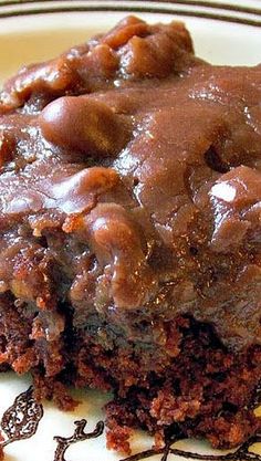 a close up of a piece of cake on a plate with chocolate frosting and nuts