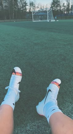 a person's legs and shoes on the ground in front of a soccer field