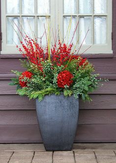 a large metal planter with red flowers and greenery in front of a purple house