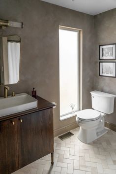 a white toilet sitting next to a window in a bathroom under a framed picture on the wall