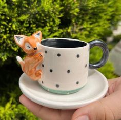 a hand holding a coffee cup with a fox figurine on it