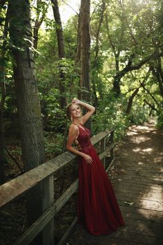 a woman in a long red dress leaning on a wooden fence and posing for the camera