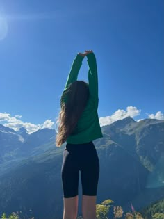 a woman standing on top of a mountain with her arms in the air