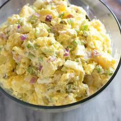 a glass bowl filled with potato salad on top of a wooden table next to a spoon