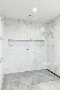 a bathroom with marble walls and flooring, shower stall and glass door to the bathtub