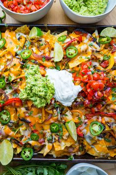 a tray filled with nachos, salsa and guacamole next to two bowls