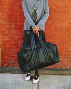 a woman holding a black bag in front of a brick wall