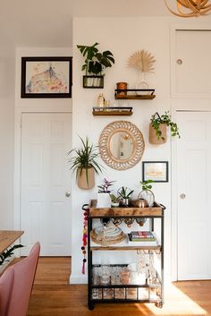 there is a shelf with plants and pictures on the wall above it in this room