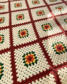 a crocheted blanket is laying on the floor next to a tablecloth that has red, yellow and green flowers