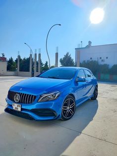 a blue mercedes cla is parked in front of a building with the sun shining on it