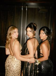 three beautiful young women standing next to each other in front of a door wearing evening dresses