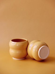 two yellow vases sitting next to each other on a brown surface with an orange background