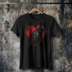 RAVEN'S BLACK T-SHIRT - Heart Black Raven Graphic Shirt, Black Crow Shirt, Gothic Raven Shirt, Gothic Halloween Tee, Gothic Fashion Tshirt This piece of art speaks to the unconventional souls who embrace the beauty of the dark and the profound intensity of their emotions. It's a hauntingly romantic reminder that love can flourish in the most unexpected places.  This just might be the softest and most comfortable women's t-shirt you'll ever own. Combine the relaxed fit and smooth fabric of this t Black Emo T-shirt For Halloween, Gothic Black T-shirt For Halloween, Emo Short Sleeve Tops For Halloween, Black Graphic Tee For Alternative Fashion, Emo Style Short Sleeve Tops For Halloween, Black Tops With Heart Graphic And Short Sleeves, Black Short Sleeve Top With Heart Graphic, Black Short Sleeve Top For Halloween, Black Gothic T-shirt For Streetwear