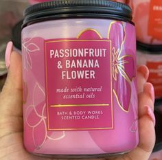 a person holding a jar of pink flower scented candle in front of some other candles