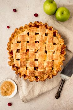 an apple pie sitting on top of a table next to two apples and a knife