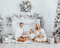 a family sitting on the floor in front of christmas trees with presents and gifts around them