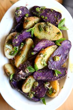 a white bowl filled with purple potatoes covered in seasoning on top of a wooden table