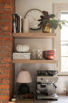 a shelf with books, cups and other items on it next to a lamp in the corner