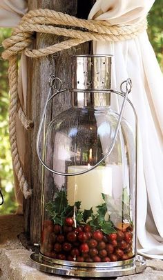 a candle and some berries in a glass container on a wooden post with white drapes