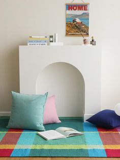 there is a book on the floor next to some pillows and a fire place in the corner