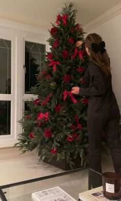 a woman is decorating a christmas tree in the living room with red flowers on it