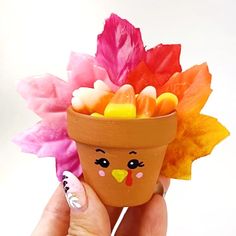 a hand holding a fake flower pot with candy in it's mouth and leaves sticking out of the top