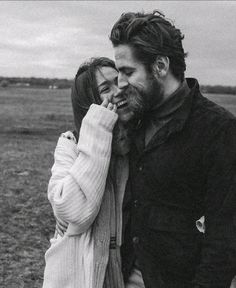 a man and woman standing next to each other in a field with one holding the other's face