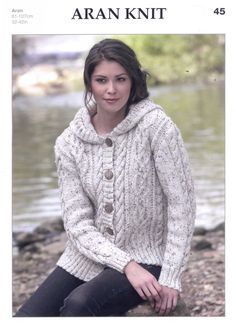 a woman is sitting on the rocks wearing a sweater