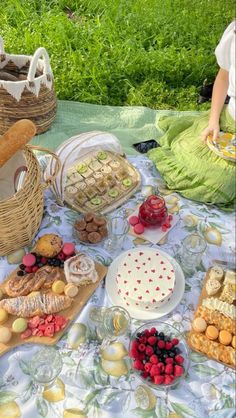 a woman sitting at a picnic table filled with food and desserts next to a basket full of fruit