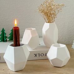 three white ceramic vases with a candle in them on top of a wooden table