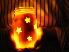 a person holding a jar filled with liquid and glowing stars on the inside, in front of a dark background