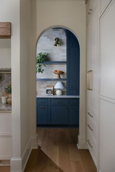 an arched doorway leads to a kitchen with blue cabinets and marble counter tops, along with wooden flooring