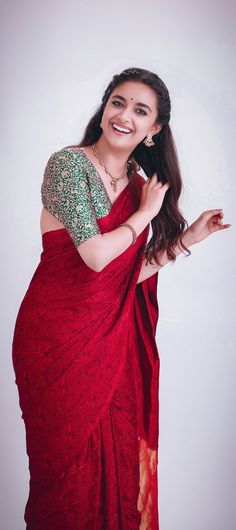 a woman in a red sari smiling and holding her hand out to the side